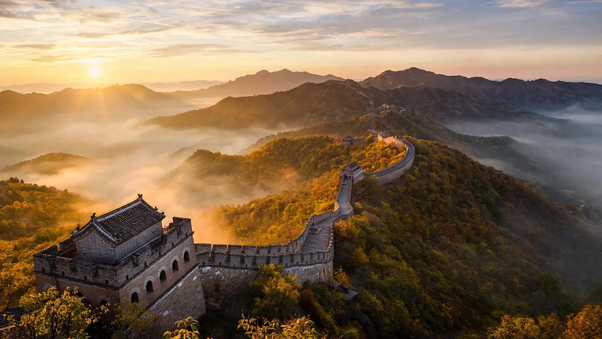 The Great Wall winding over forested mountain ridges in golden morning mist